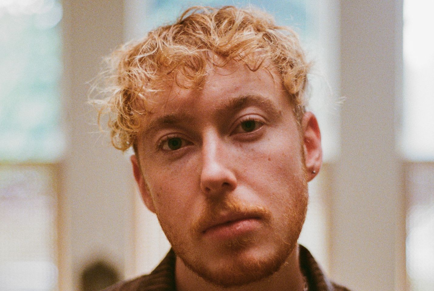 A close up image of a person with blonde curly hair and one ear piercing